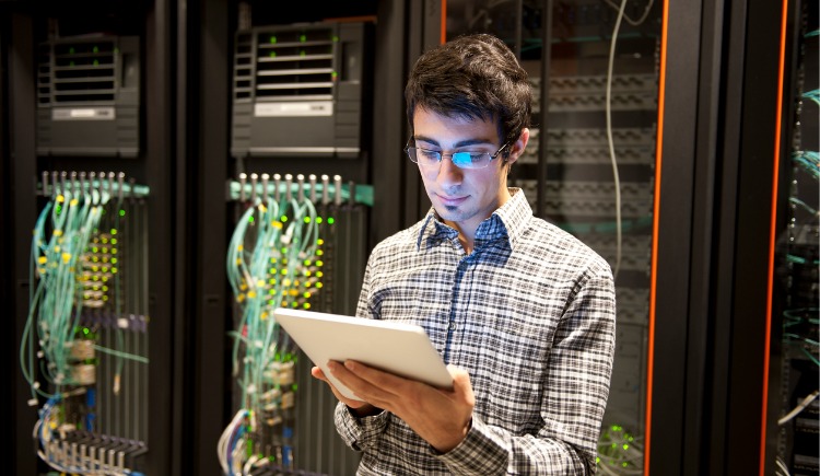 Man with glasses holding tablet in server room