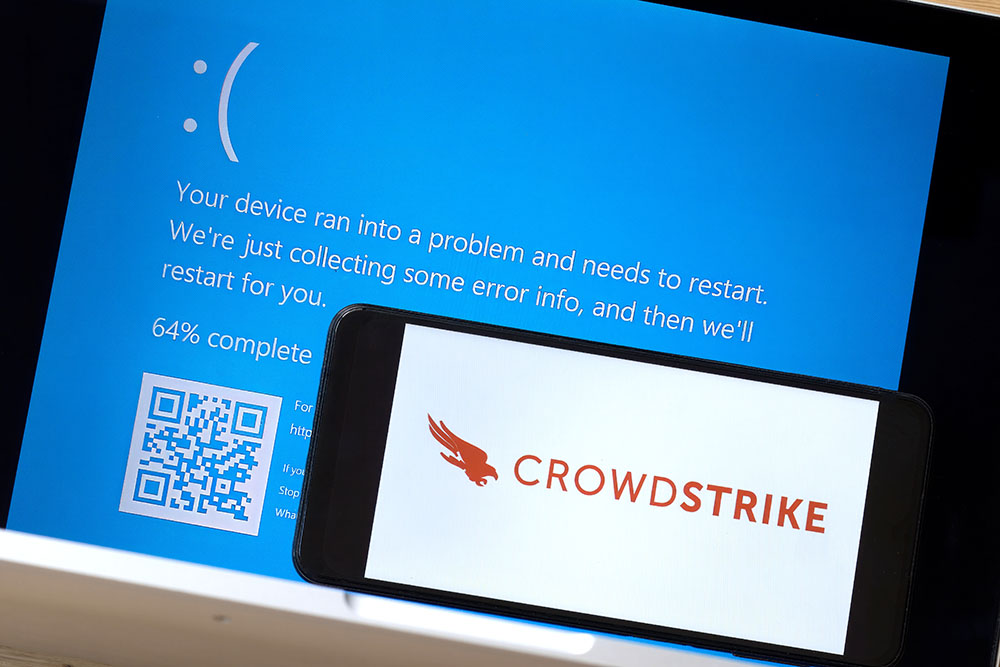 A computer screen shows a blue error message, while a smartphone in the foreground displays the CrowdStrike logo.