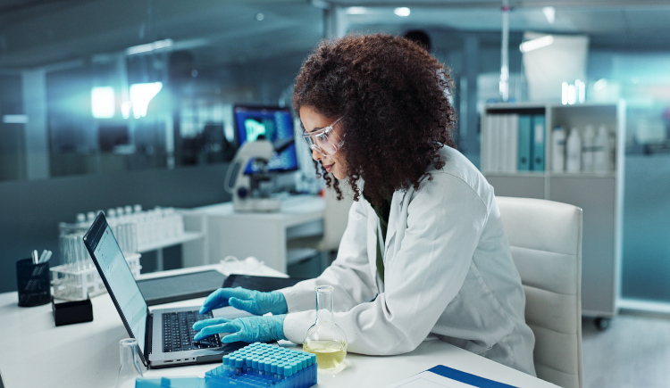 Woman lab personnel in lab coat working on laptop