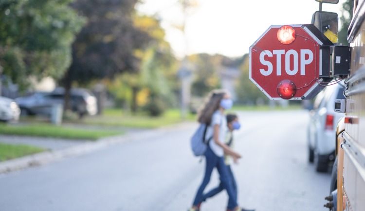 Blinking stop sign on school bus as kids cross street in background