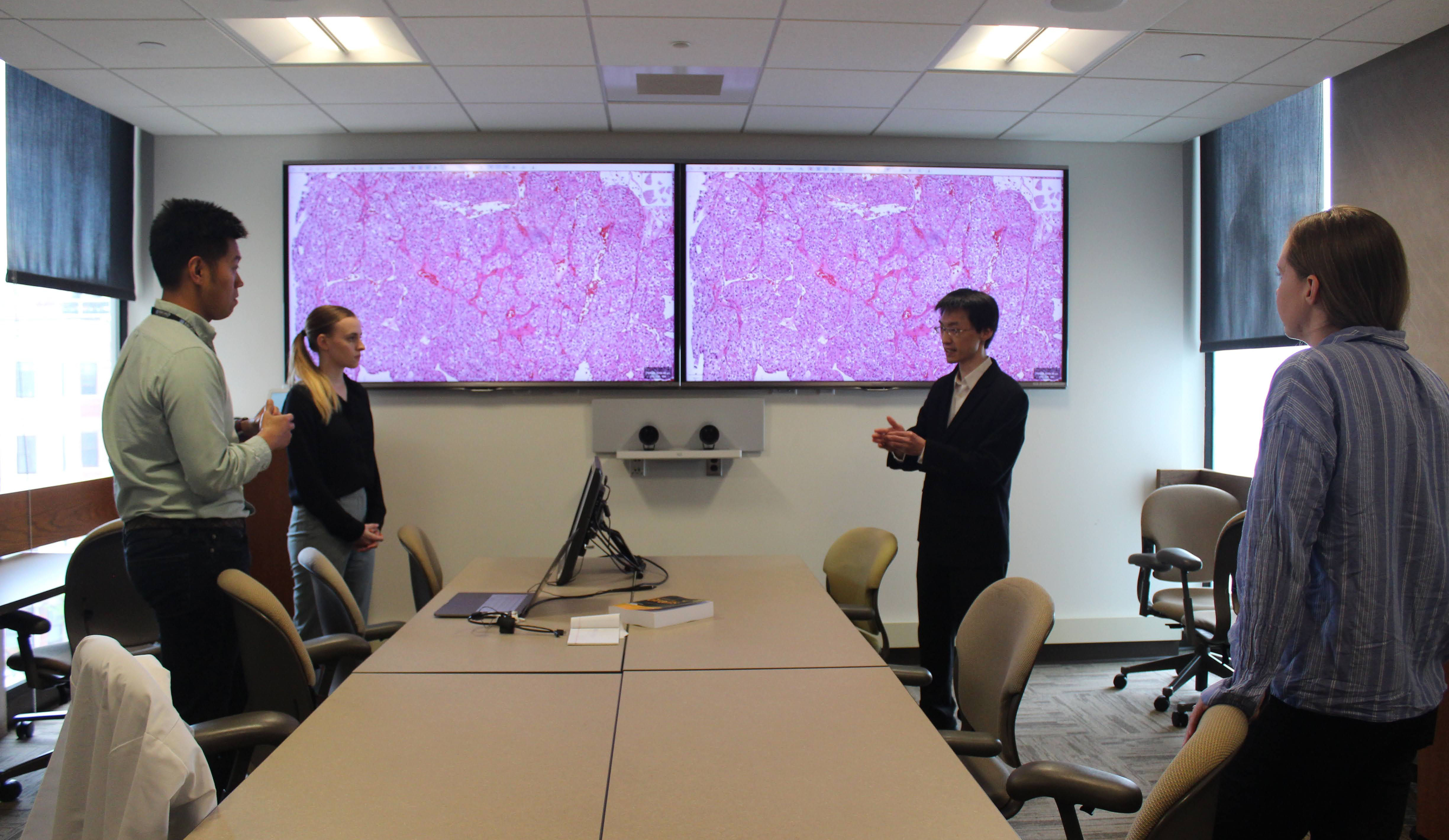Dr. Kun-Hsing Yu meets with members of the Yu Lab in front of two screens, which show image samples.