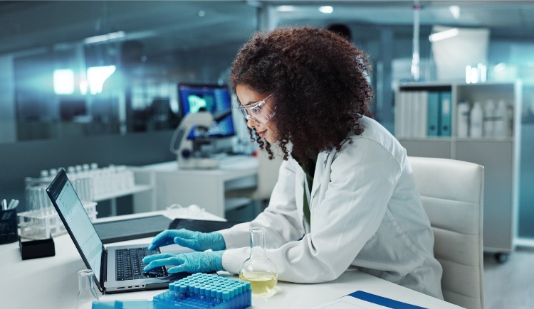 Scientist woman typing on laptop with test tube next to her